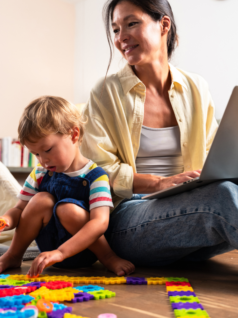 Mom on laptop with child playing by her side with a puzzle. Mom is working out ABA costs
